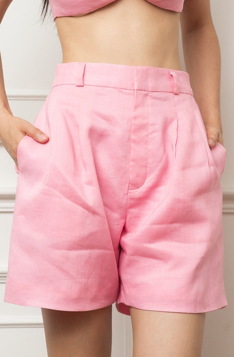 Woman wearing a pink bow top and shorts set against a white wall.