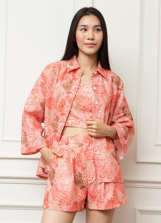 Woman wearing a pink floral pajama set against a white paneled wall.