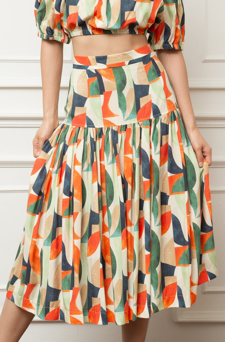 Woman wearing a colorful off-shoulder dress against a white paneled wall.